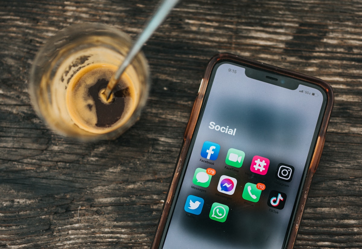 A phone showing social and advertising apps beside a coffee on a desk